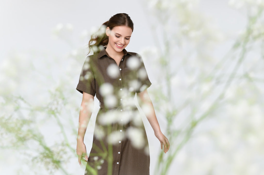 Woman in brown linen dress with white flowers in front of her.