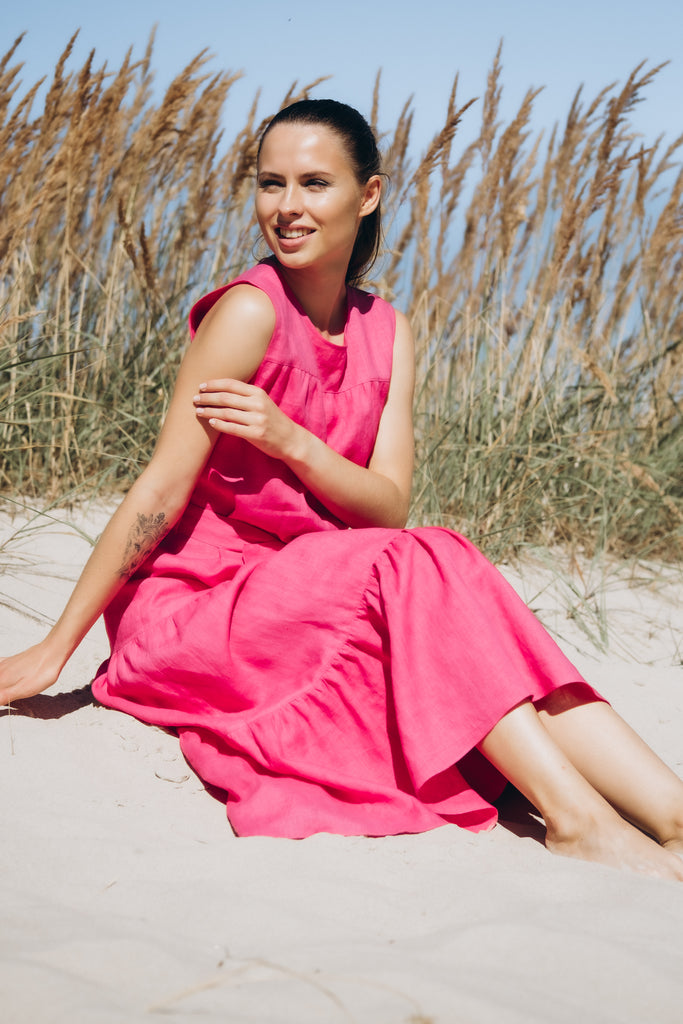 Woman sitting in a sand wearing a pink linen dress.