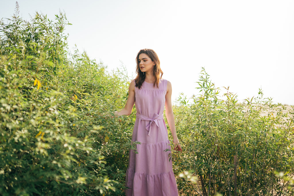 Woman standing between the trees in a violet linen dress.