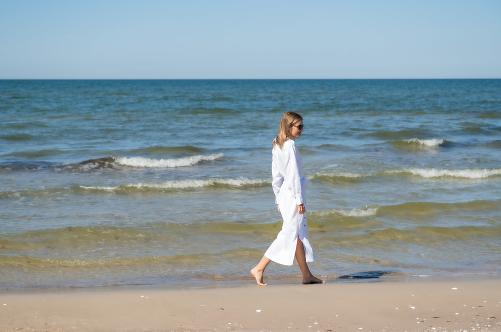 Woman walking on the beach in a white linen dress.