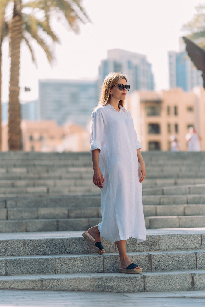 Woman walking down the stairs in a white linen dress.